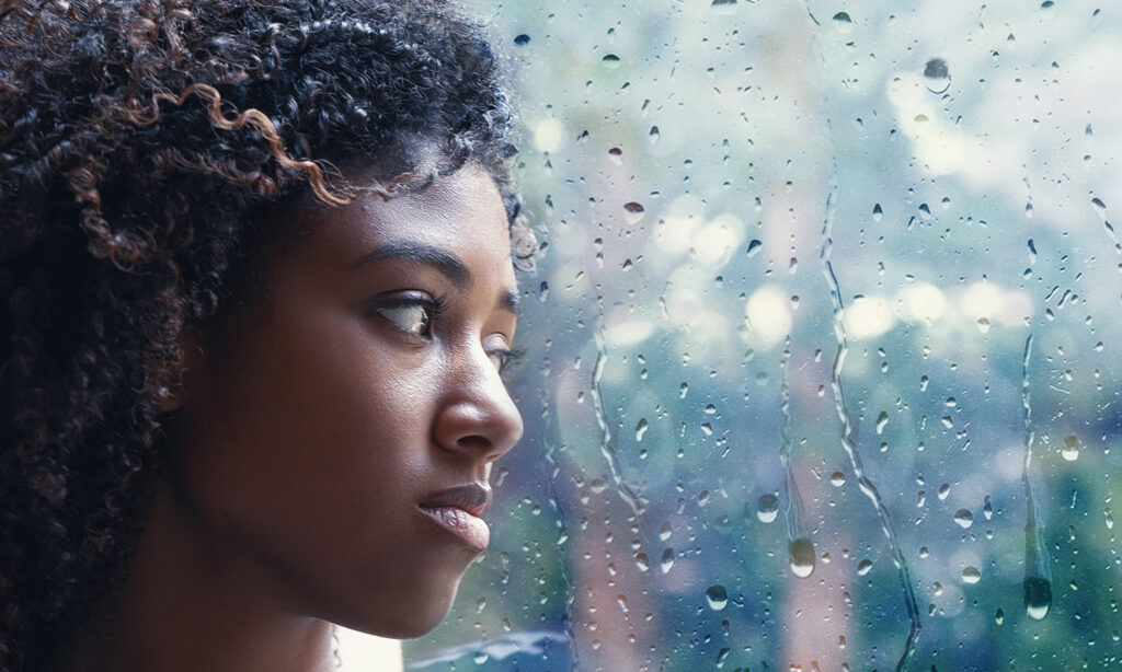 young-woman-looking-out-through-rain-covered-window